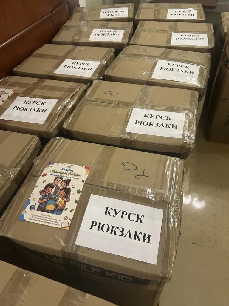 Коробки с надписью «Курск. Рюкзаки» и наклейкой акции с нарисованной семьёй
