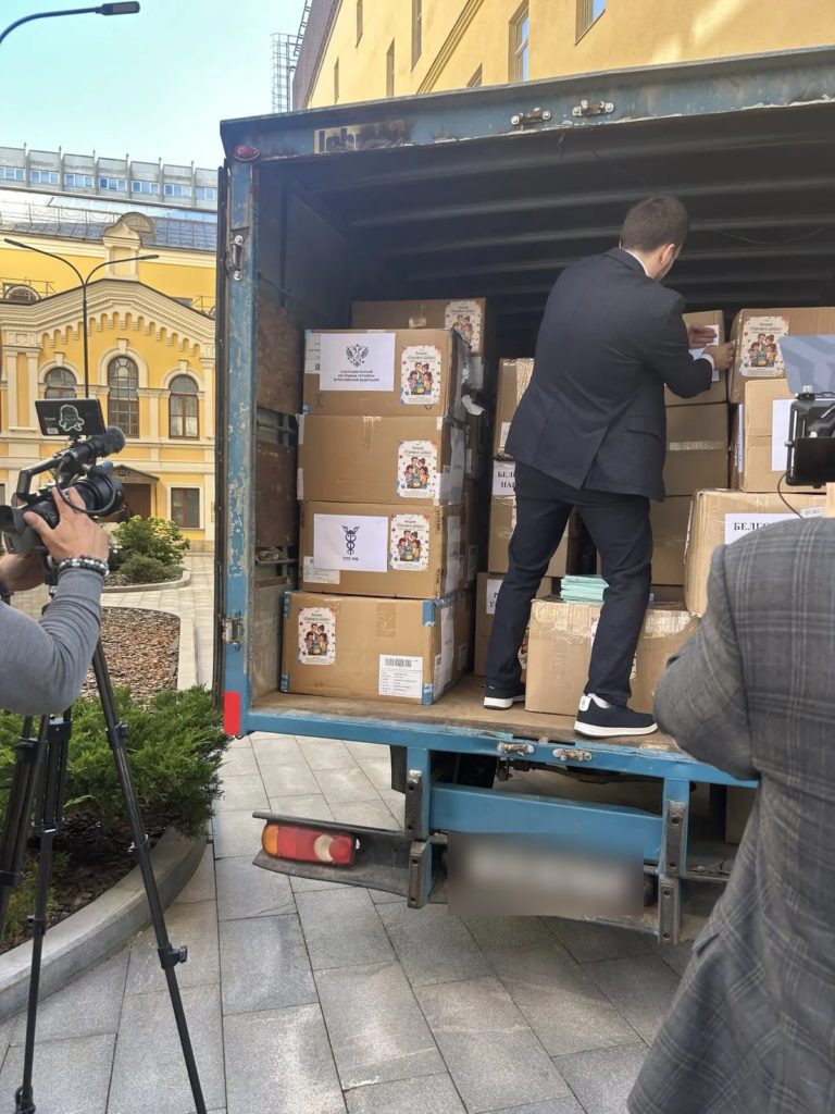 Мужчина в костюме расставляет коробки в кузове грузовика, рядом оператор с камерой